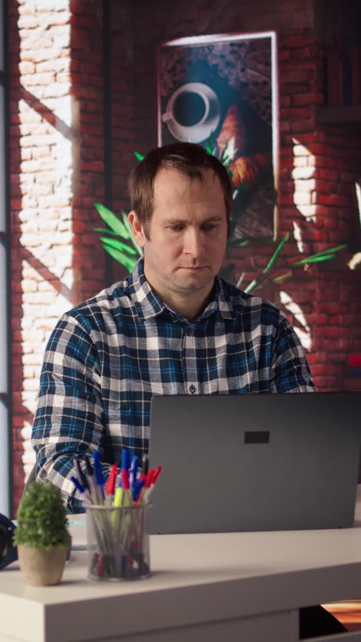 Vídeo vertical: Freelancer em home office sentado à mesa e digitando no teclado do laptop.