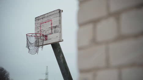 old basketball hoop with torn net hanging in wind and peeled off paint