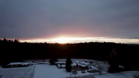 Levantándose-Lentamente-A-Medida-Que-Sale-El-Sol-Sobre-Un-Campo-Cubierto-De-Nieve-En-Un-Barrio-Suburbano,-Aéreo