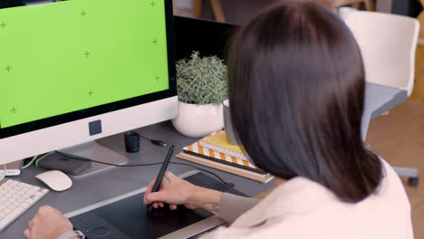 Back-View-Of-A-Female-Graphic-Designer-Using-Digital-Drawing-Tablet-And-Looking-At-Monitor-With-Green-Screen-In-An-Animation-Studio