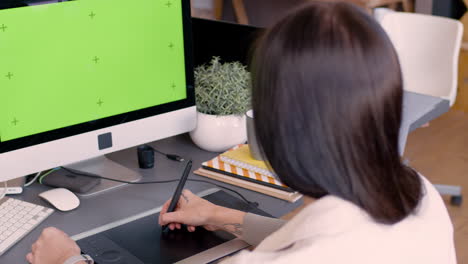 back view of a female graphic designer using digital drawing tablet and looking at monitor with green screen in an animation studio