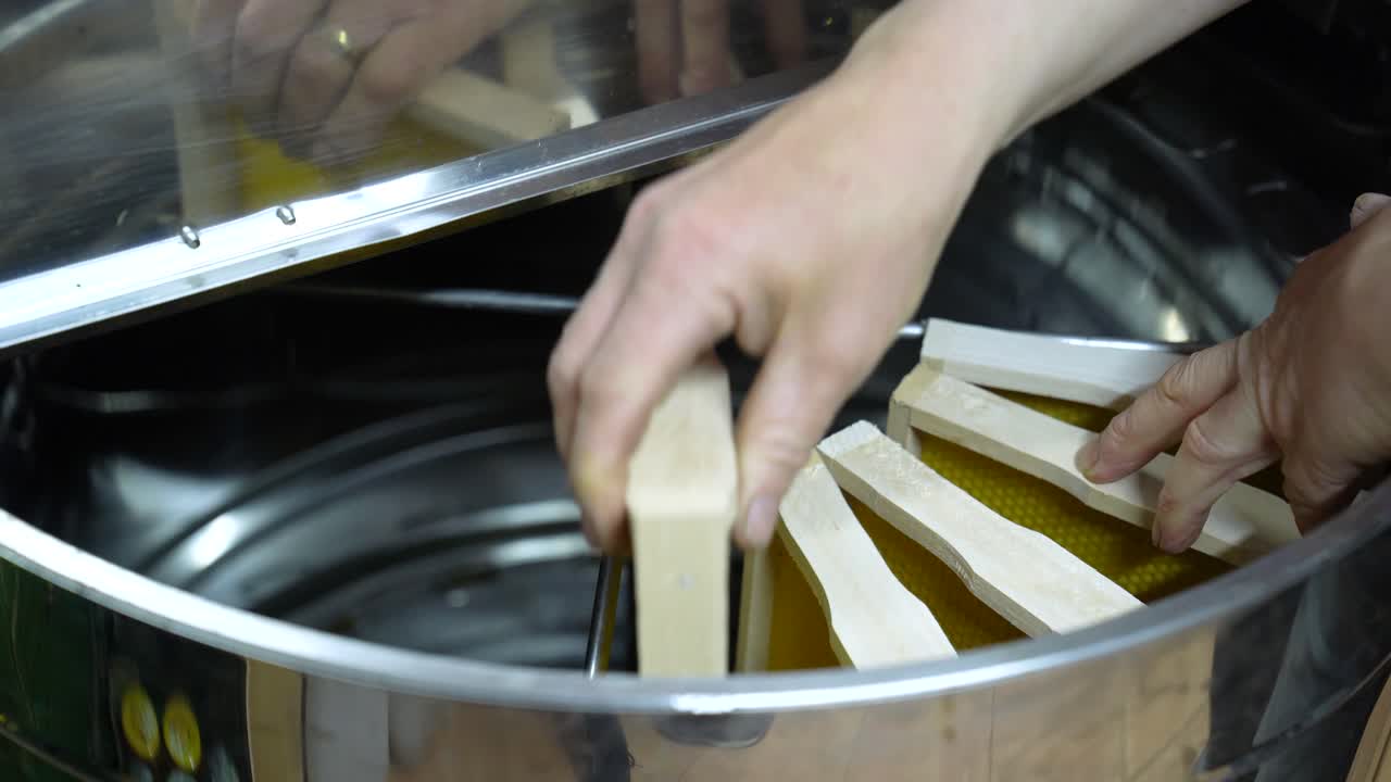 Person Putting The Hive Frames On Cylindrical Honey Extractor Machine. - closeup shot