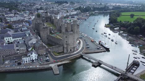 Ancient-Caernarfon-castle-Welsh-harbour-town-aerial-view-medieval-waterfront-landmark-descending-birdseye