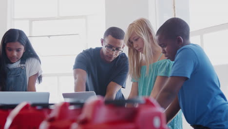 students with male teacher in after school computer coding class learning to program robot vehicle