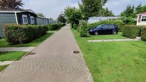 moving shot of a man walking across a trailer park. cars are parked and it's a sunny day.