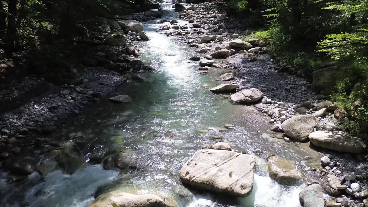 ターコイズ色の山の川が流れる森をゆっくりと飛行するドローン。