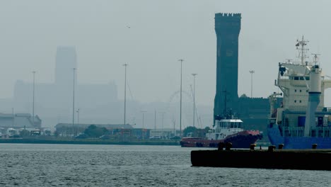 Tugboat-pushing-a-big-ship-into-docks-and-past-dock-gates-on-a-hazy-day