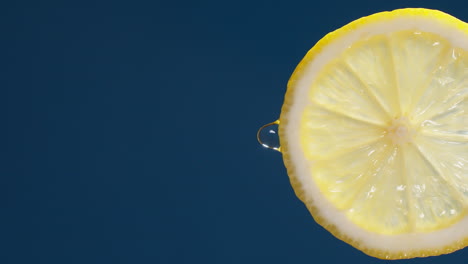 vertical of slow motion macro shot of flowing water from lemon slice on blue-black background