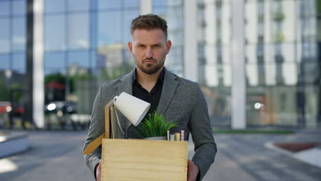 man holding cardboard box outside office building - job loss