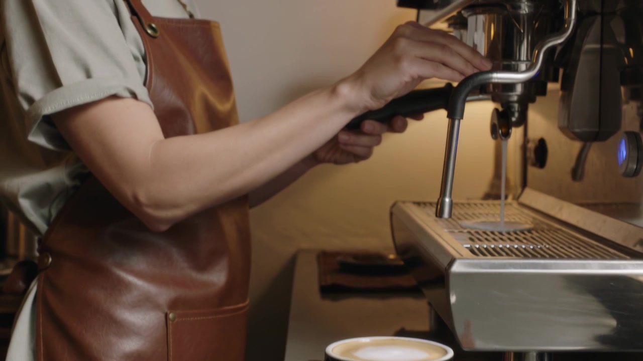 Con la tazza pronta, un barista con grembiule afferra il portafiltro alla macchina da caffè espresso, preparando un espresso.