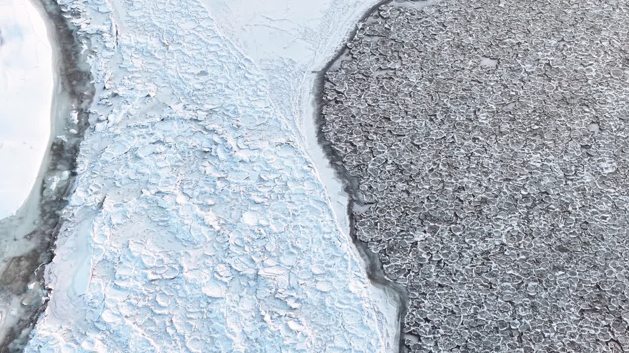 Detailed macro view of contrasting ice and snow textures. The white snowy surface meets rugged, icy terrain, showcasing intricate patterns in cold, natural lighting