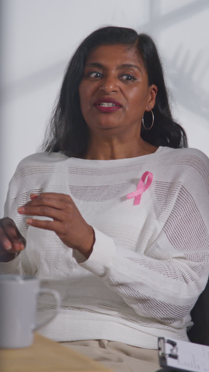 Vertical Video Of Mature Woman Wearing Pink Breast Cancer Awareness Ribbon Meeting And Talking At Therapy Support Group For Cancer Treatment Patients With Counsellor 1