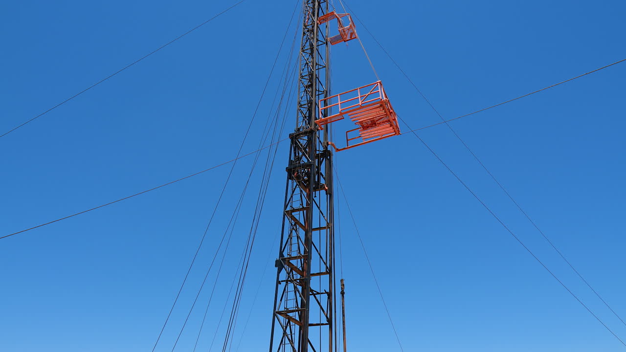 Three men standing at the truck with the derrick for oil drilling. Low angle view at the tower for boring resources.
