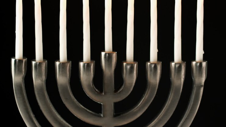Tilt shot of Jewish menorah candelabrum with lit candles against black background