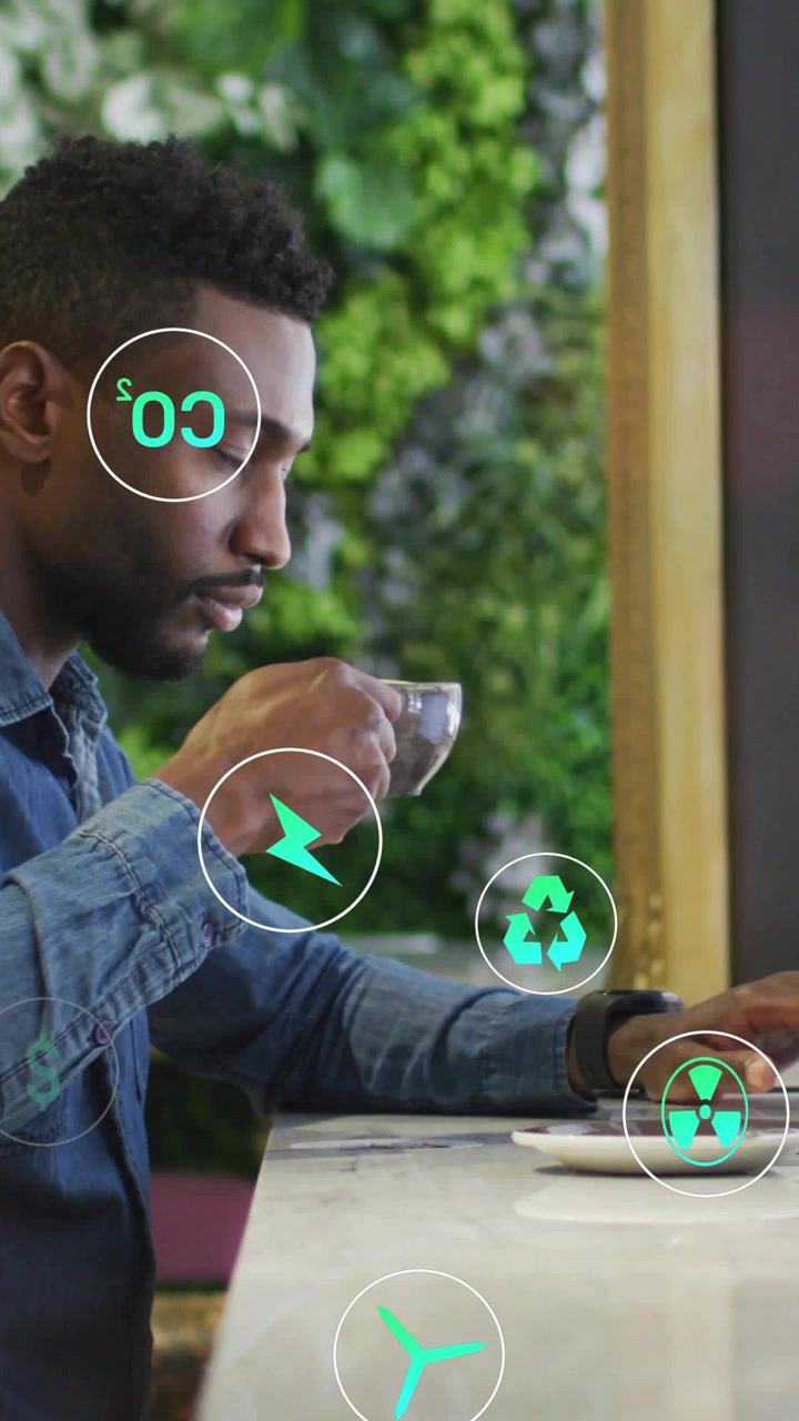 Vertical video: Man sipping drink, using laptop, green icons appearing over screen showing eco data
