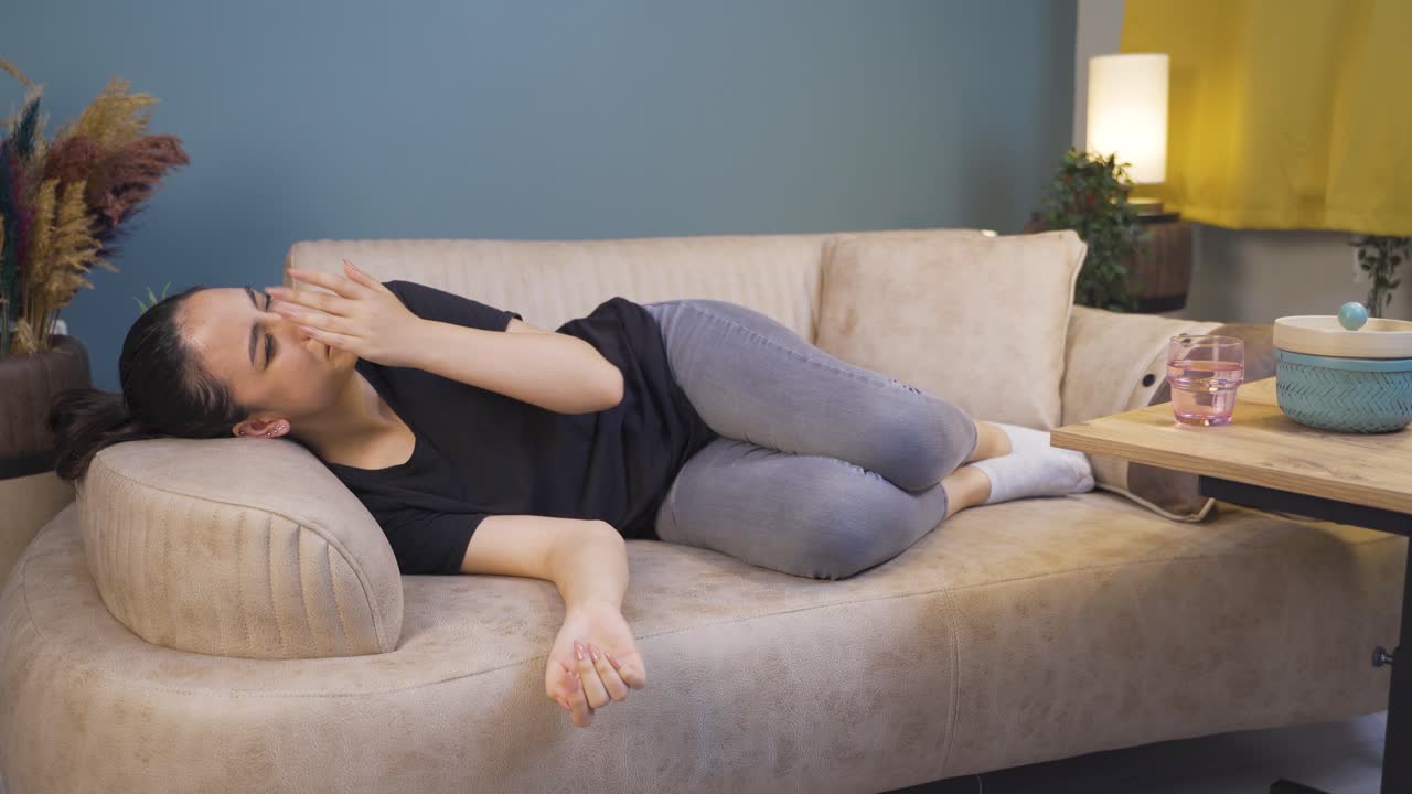 소파에 누워 있는 젊은 여성이 울고 있습니다.