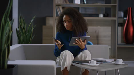 Serious-african-american-ceo-woman-surfing-tablet-answering-phone-call-in-office