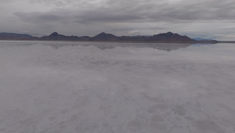 drone fast low approach over bonneville salt flats with water reflecting the sky and clouds