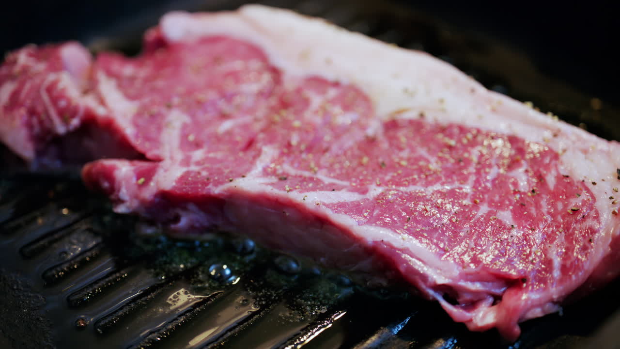 Fresh raw steak sizzling on a hot grill pan with visible seasoning and cooking oil