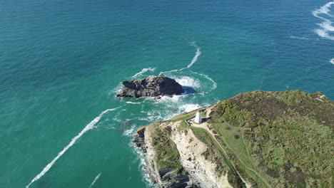 gull rock surrounded by turquoise blue sea in portreath cornwall with view of pepperpot on a summer day - aerial