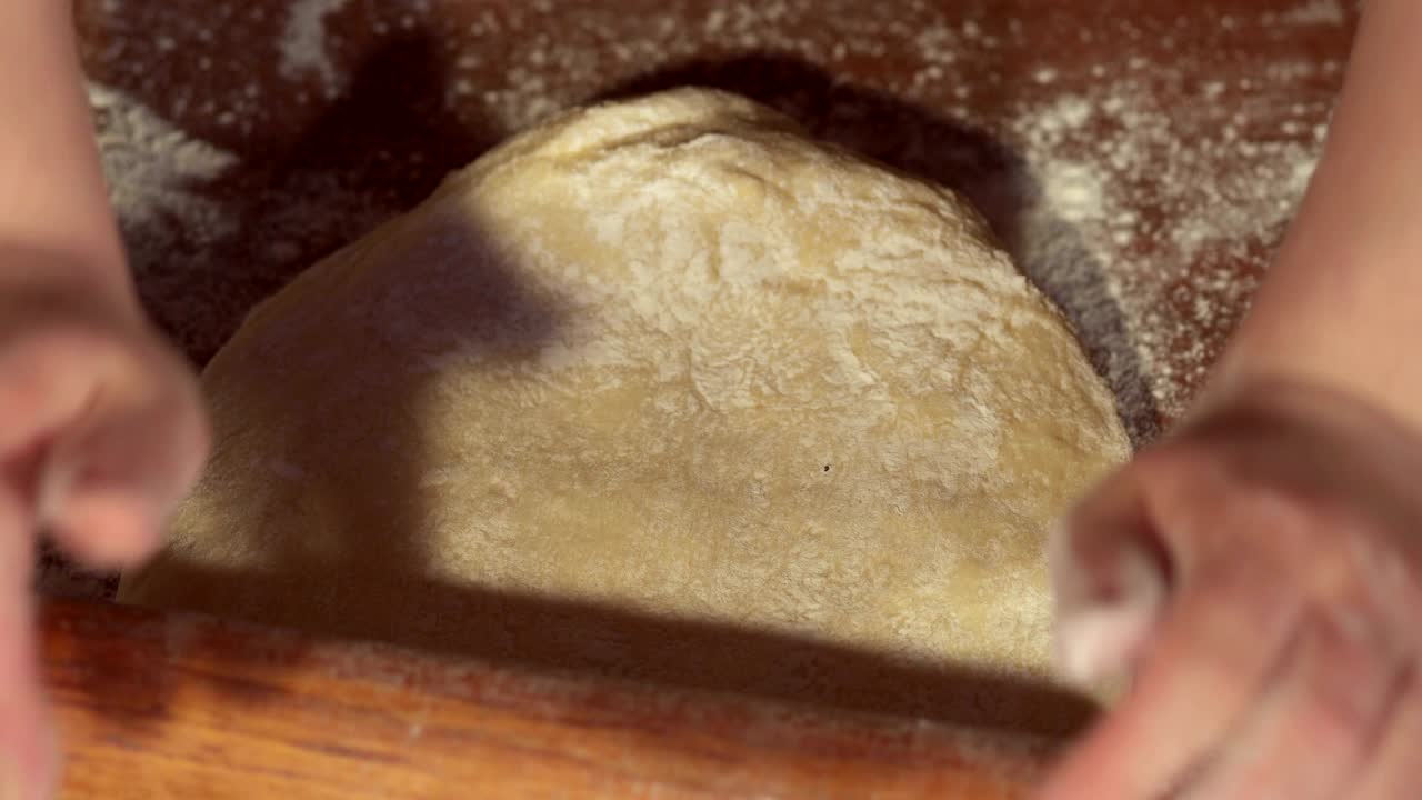 Cook's hands rolling out dough on wooden board.