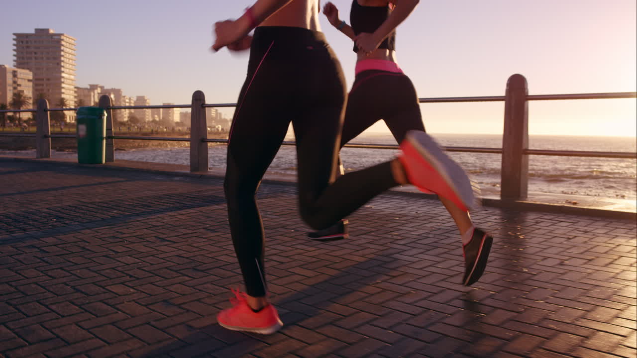 Two athletic woman running outdoors slow motion on promenade at sunset near ocean enjoying evening run