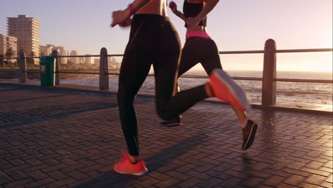 Zwei-Sportliche-Frauen-Laufen-Im-Freien-In-Zeitlupe-Auf-Der-Promenade-Bei-Sonnenuntergang-Am-Meer-Und-Genießen-Den-Abendlauf