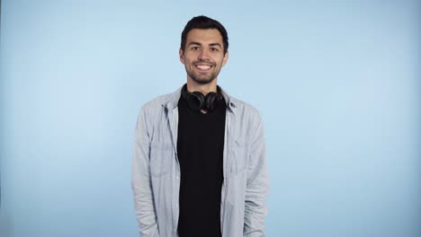 Cropped-shot-of-happy-excited-handsome-caucasian-man-in-blue-shirt-standing,-looking,-toothy-smile,-surprised-and-waving-his-hand-and-greeting.-Indoor-studio-shot-isolated-on-blue-wall-background