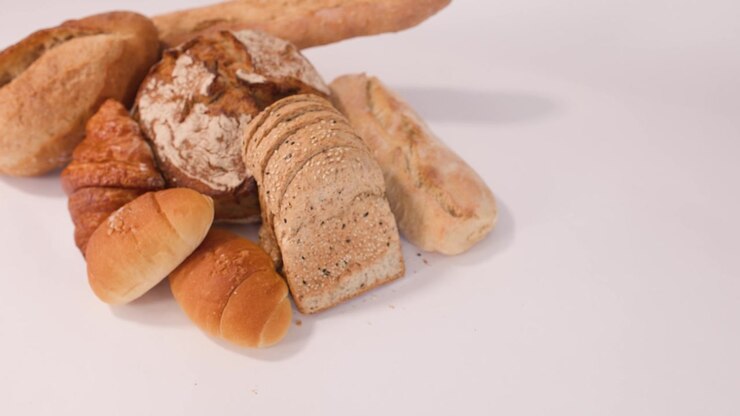 Static high-angle shot of sourdough, baguettes, and croissants arranged on a plain white surface.