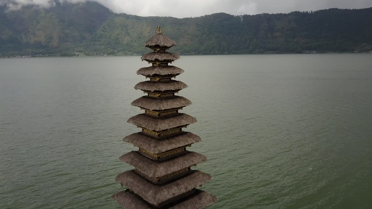 Clip de dron aéreo mostrando una órbita parcial alrededor de la pagoda del Templo Ulun Danu Beratan en el Lago Beratan, con agua tranquila y montañas al fondo en Bali, Indonesia