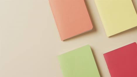 overhead view of colourful notebooks arranged on beige background, in slow motion