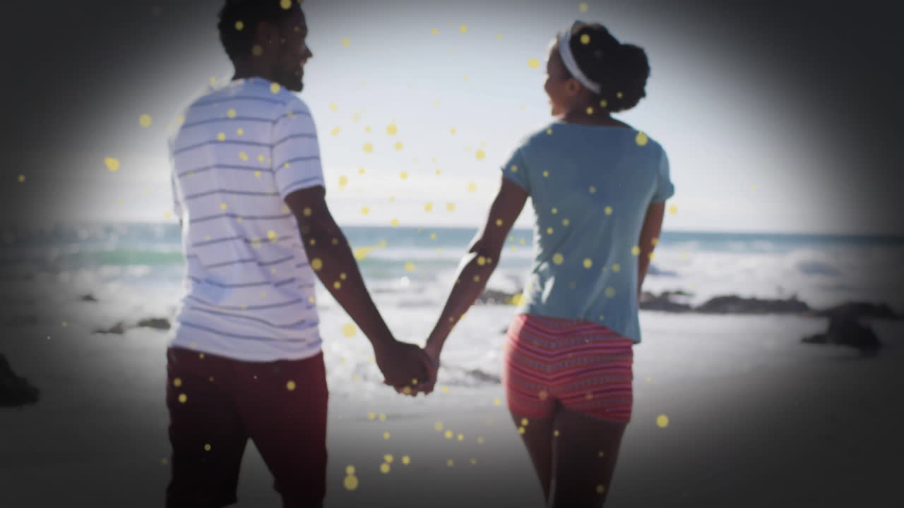 Couple holding hands walking on beach with golden sparkles animation overlay