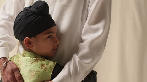 a father and son embrace, the boy wearing a turban.