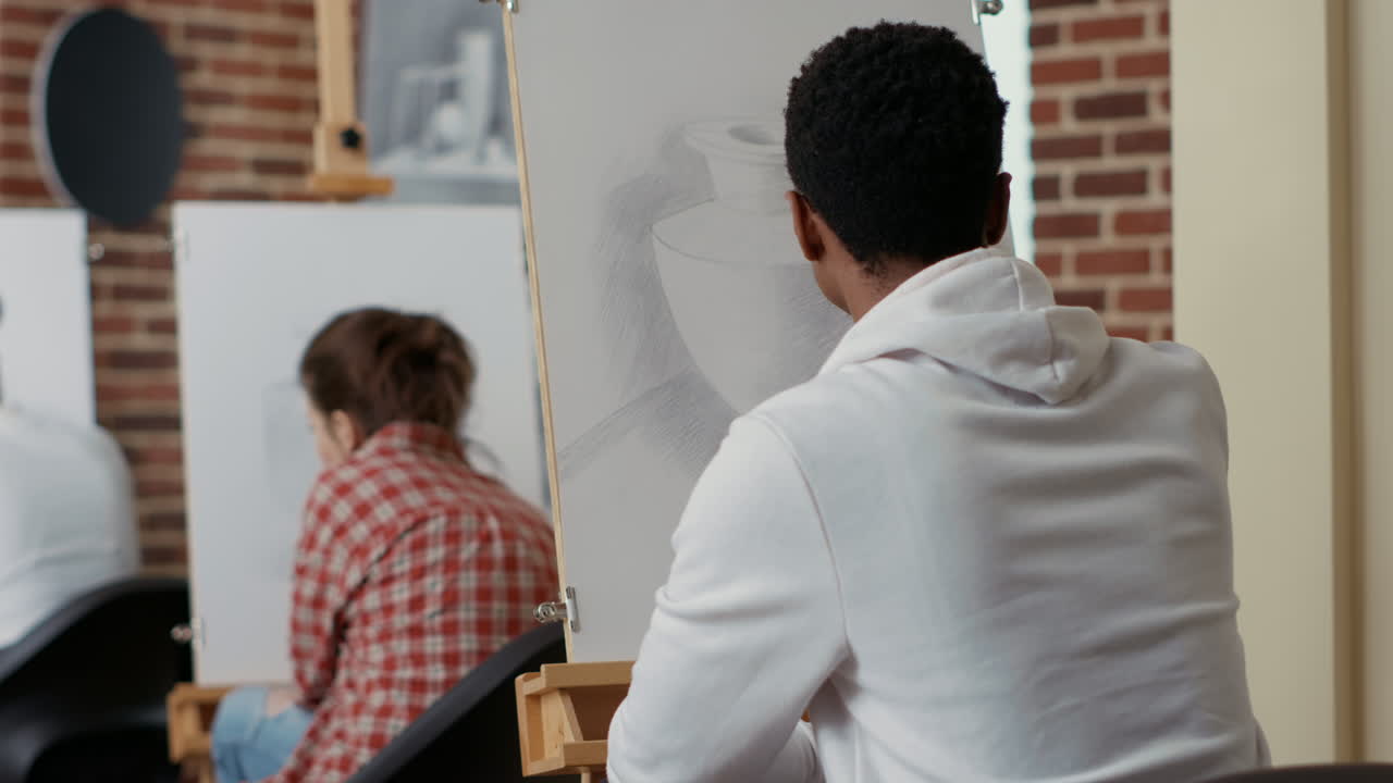 Young student looking at vase model to draw sketch on canvas