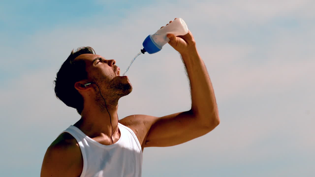 hombre atlético rehidratándose con agua en la playa