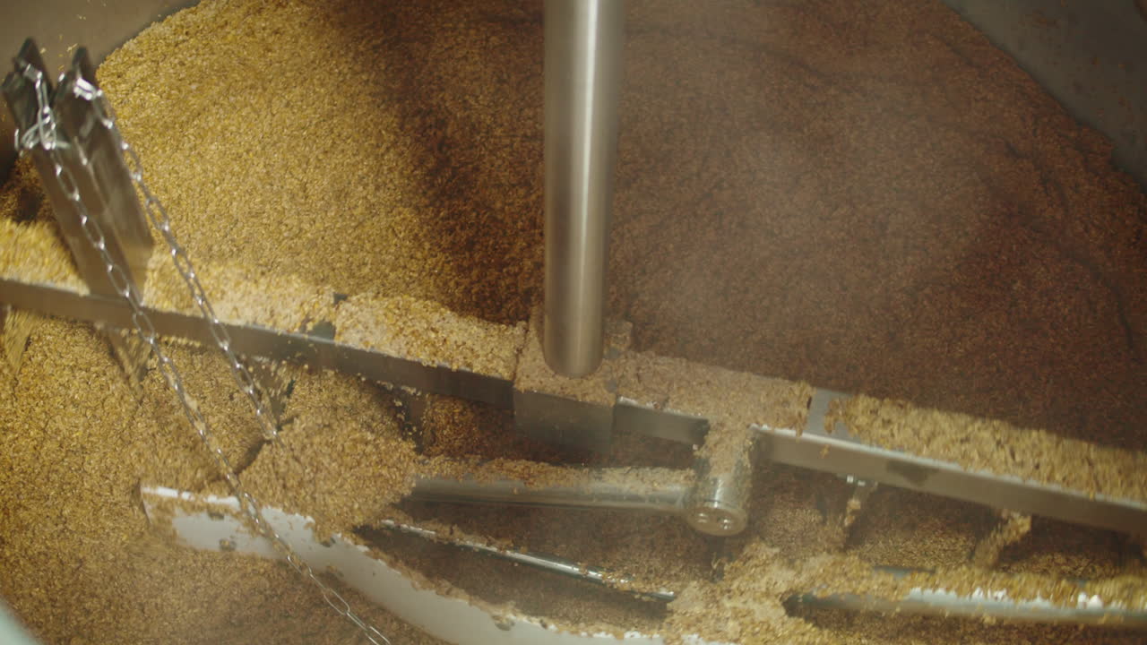 Craft beer production factory, brewery manufacture. Putting barley malt grains in conveyor close-up. Brewing, cooking alcohol in metal vats bottles