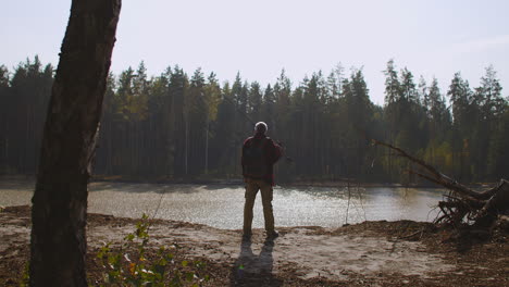 Der-Fischer-Lässt-Sich-Durch-Die-Naturbeobachtung-Am-Fluss-Oder-See-In-Der-Herbstsaison-Inspirieren.-Rückansicht-Eines-Mannes-Mittleren-Alters-Auf-Einer-Klippe