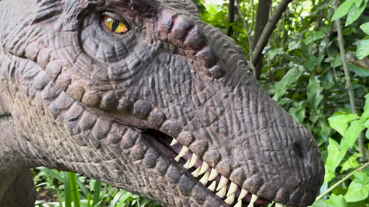 Un primo piano dettagliato di una testa di dinosauro animatronico realistica che si muove lentamente tra il fitto fogliame della foresta