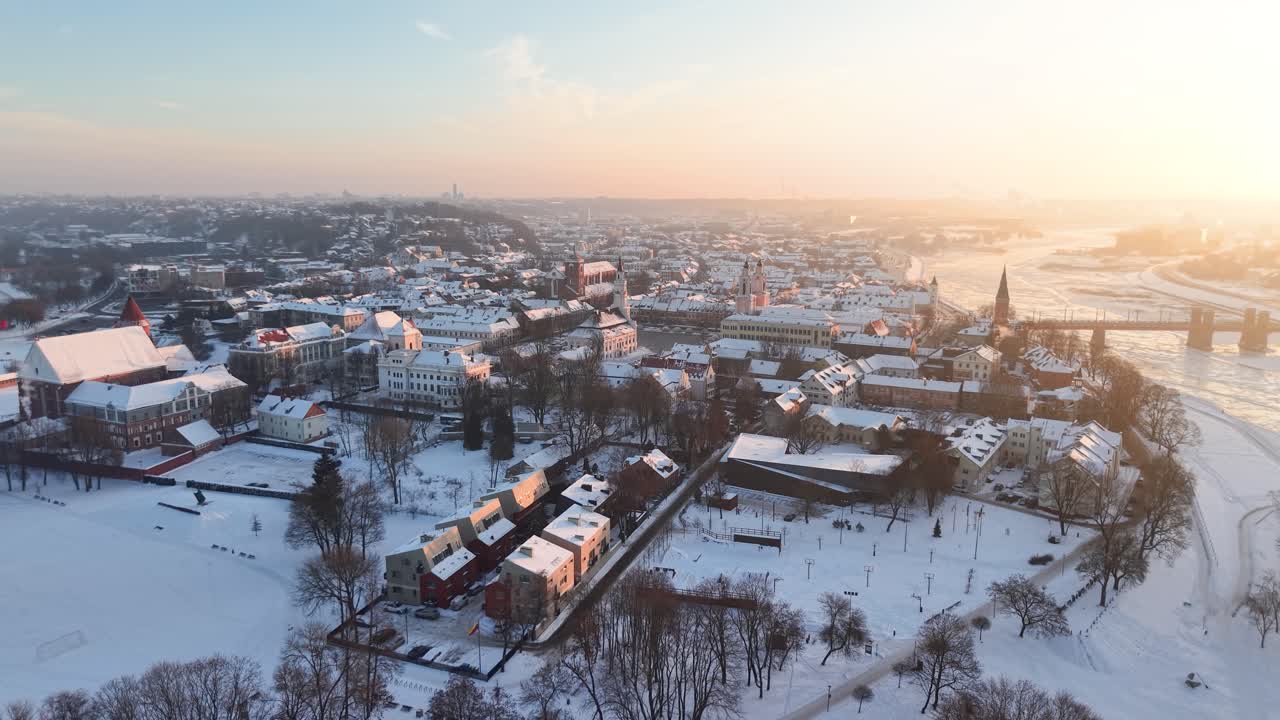 Drone-optagelser fanger Kaunas' gamle bydel dækket af sne ved solopgang og fremhæver historiske kirker og rådhuset med varmt, gyldent lys og en fredfyldt vinterstemning.