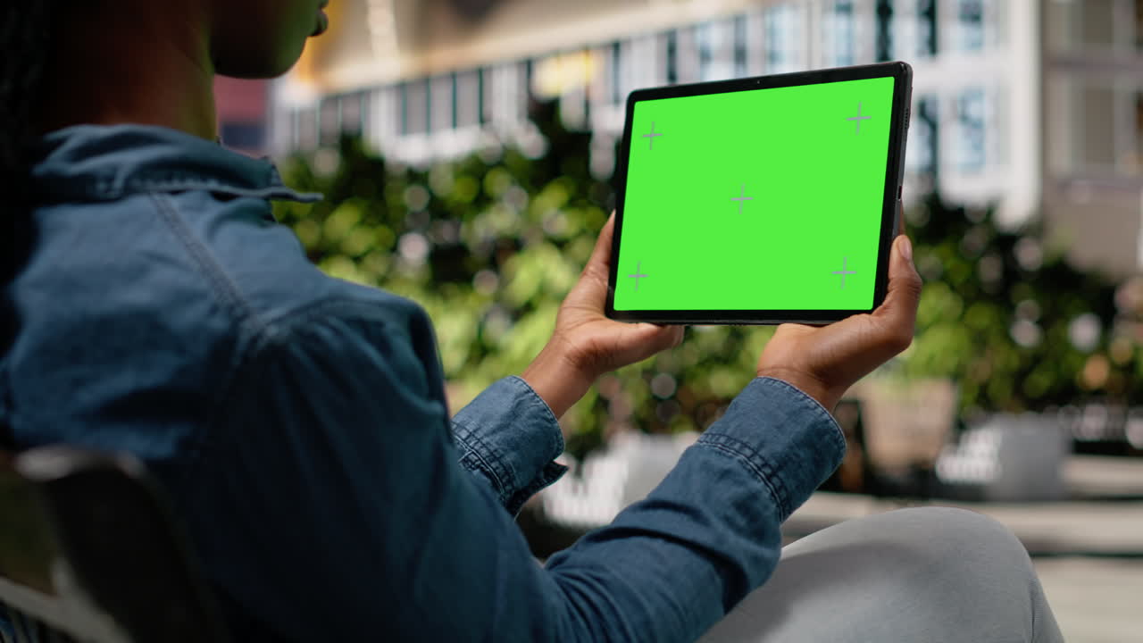 Schermo verde su tablet mostrato da una ragazza afroamericana che si rilassa in un parco in centro.