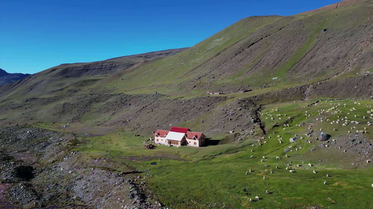 A remote mountain lodge sits below the snowy Ausangate peak in Peru. Llamas graze nearby. Stunning aerial footage of this peaceful high-altitude retreat