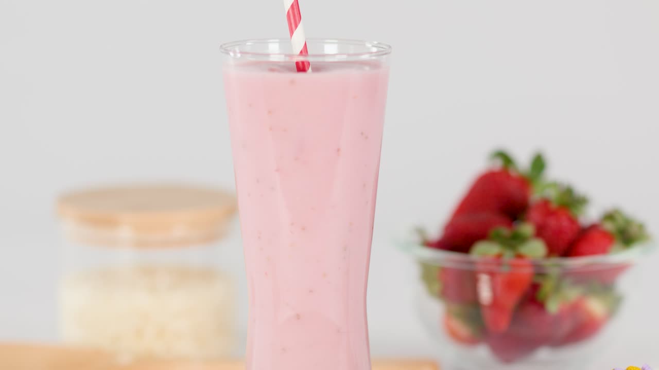 Hand inserts striped straw into creamy strawberry milkshake, bright studio lighting, clean background