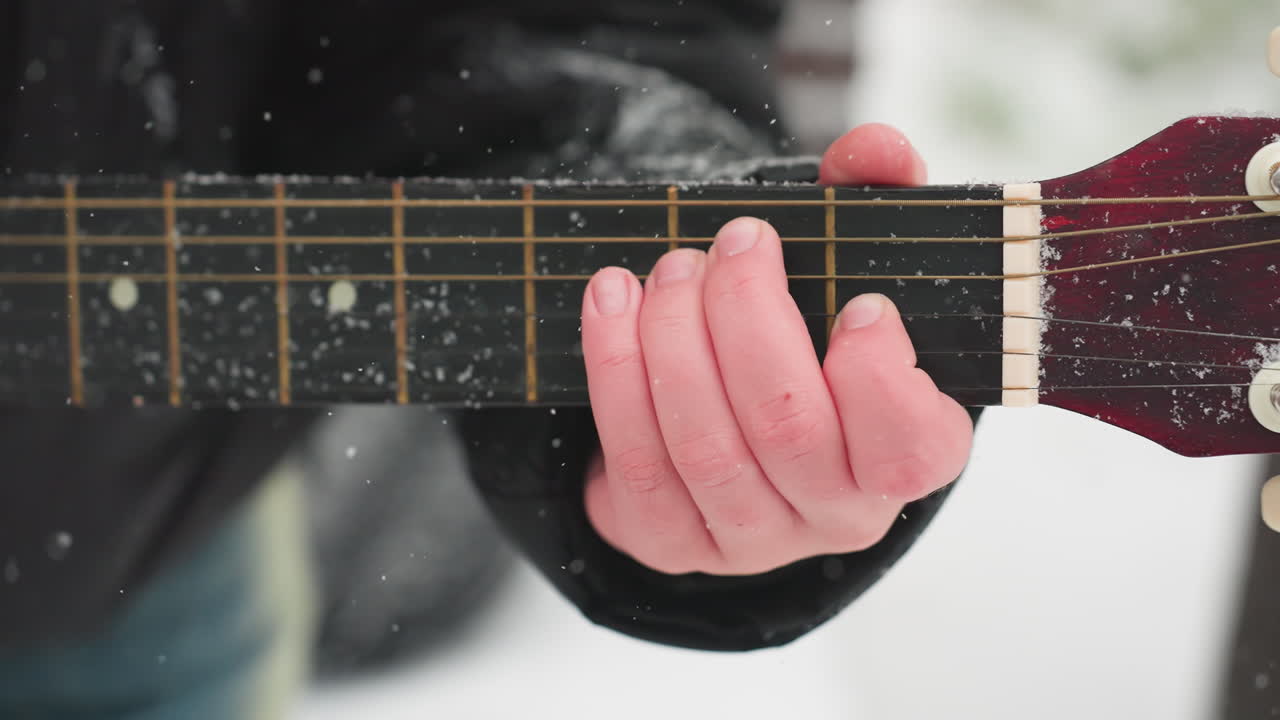 primer plano de la mano tocando la guitarra en cuerdas de polvo de nieve, mezclando la música y la belleza del invierno, mostrando la armonía artística con detalles helados en el cuello de la guitarra y el fondo blanco sereno