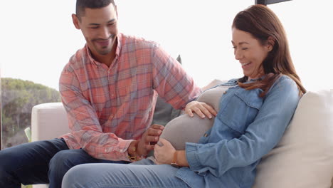 expecting couple sitting on couch, man touching pregnant woman's belly lovingly