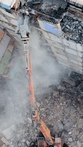 aerial view of excavator at a construction site destroys an old multi-storey building. vertical video