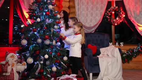 mother with two daughters decorate beautiful christmas tree in the wooden house. happy family preparing for the holiday. close look with slow movement back.