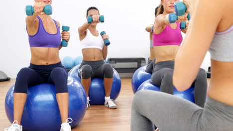 clase de fitness sentado en pelotas de ejercicio levantando pesas con las manos