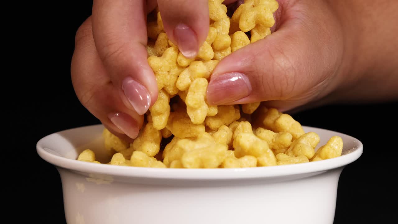 A hand reaches into a bowl of star-shaped cereal against a black background, highlighting texture and movement