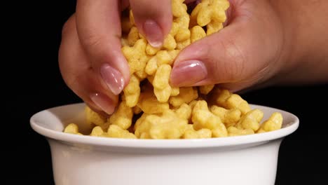 a hand reaches into a bowl of star-shaped cereal against a black background, highlighting texture and movement