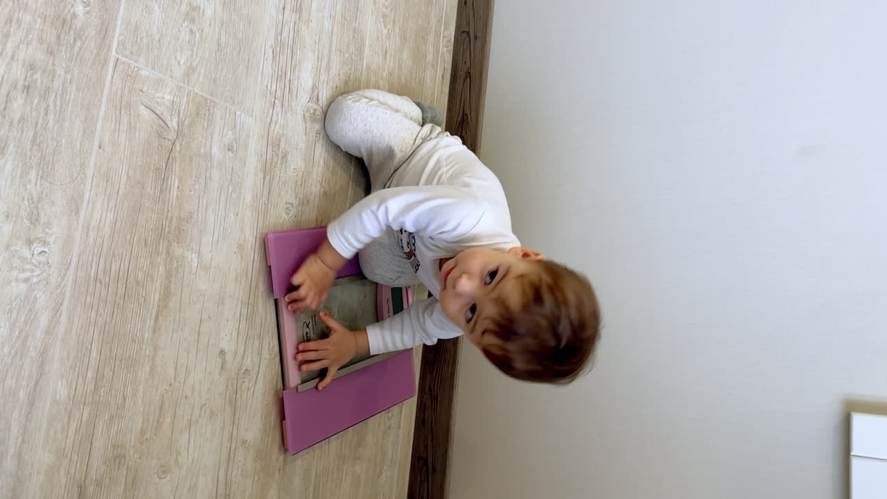 Adorable baby playing with scales on the floor. Cute little child sits on the weights looking up at camera. Vertical video.